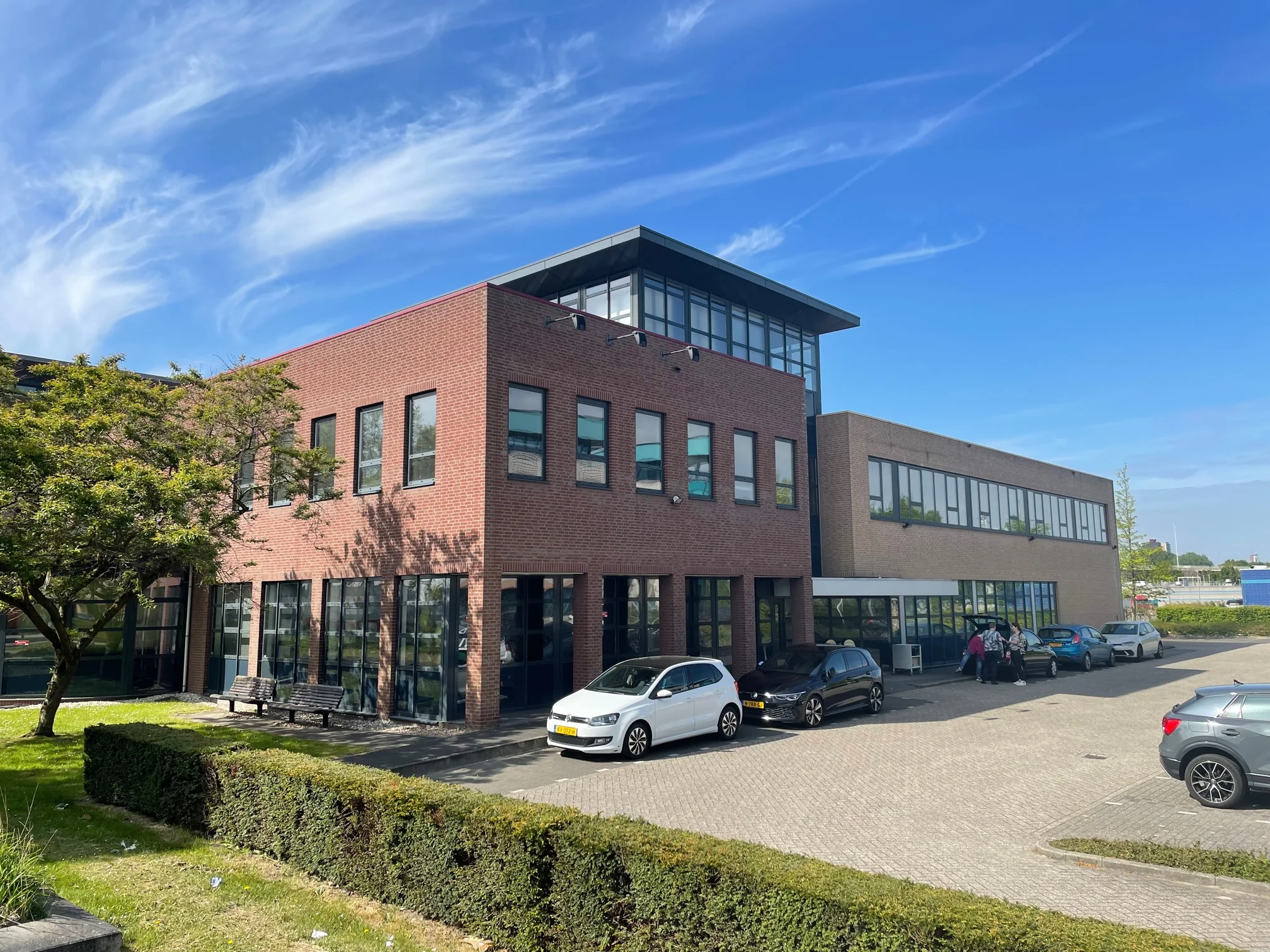 Kantoorgebouw aan de Rivium 4e Straat met geparkeerde auto's en een blauwe lucht op de achtergrond.